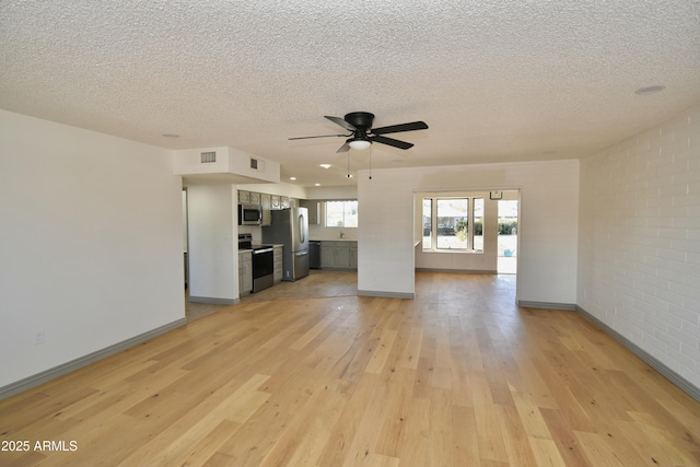 unfurnished living room with brick wall, a textured ceiling, and light hardwood / wood-style flooring