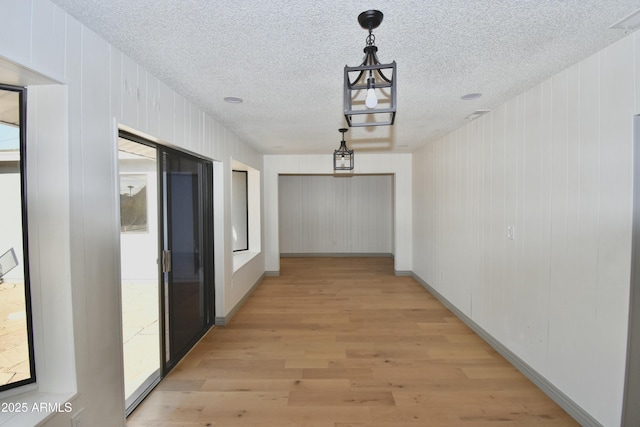 hallway featuring wood walls, plenty of natural light, a textured ceiling, and light wood-type flooring