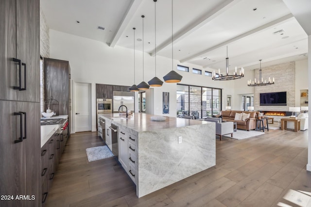 kitchen with a large island with sink, a high ceiling, a stone fireplace, sink, and stainless steel appliances