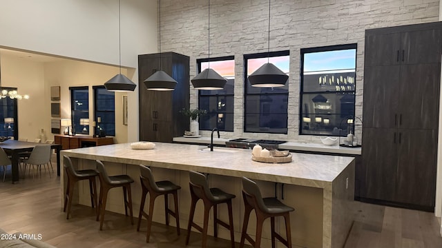 kitchen featuring a kitchen island with sink, sink, light hardwood / wood-style flooring, decorative light fixtures, and a kitchen bar