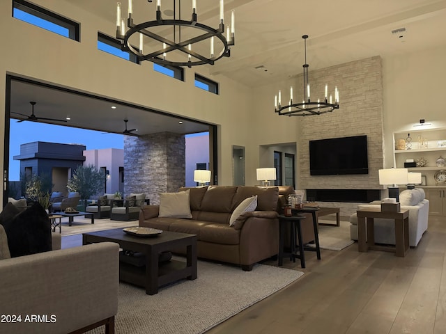 living room with a fireplace, a towering ceiling, ceiling fan with notable chandelier, and hardwood / wood-style flooring