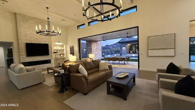 living room with ceiling fan with notable chandelier, hardwood / wood-style floors, a towering ceiling, and a stone fireplace