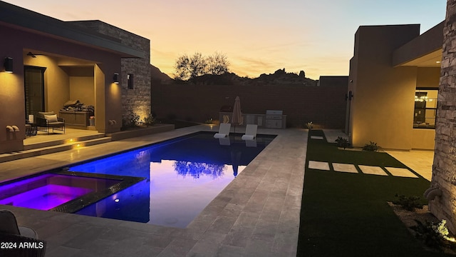 pool at dusk featuring a patio area, an in ground hot tub, and exterior kitchen