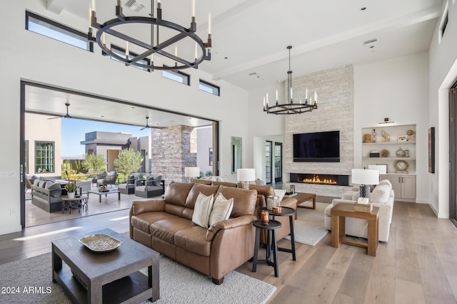 living room featuring a high ceiling, light hardwood / wood-style floors, a stone fireplace, and a healthy amount of sunlight