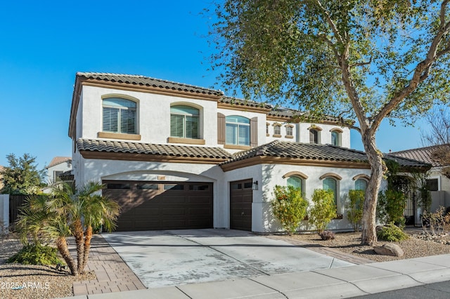 mediterranean / spanish home with an attached garage, a tile roof, concrete driveway, and stucco siding