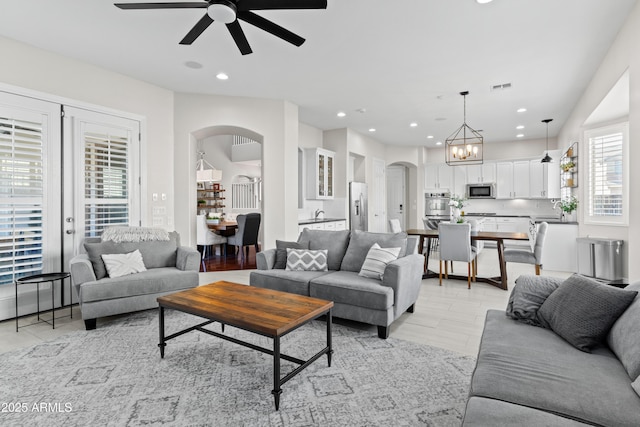 living room with light tile patterned floors, recessed lighting, visible vents, arched walkways, and ceiling fan with notable chandelier