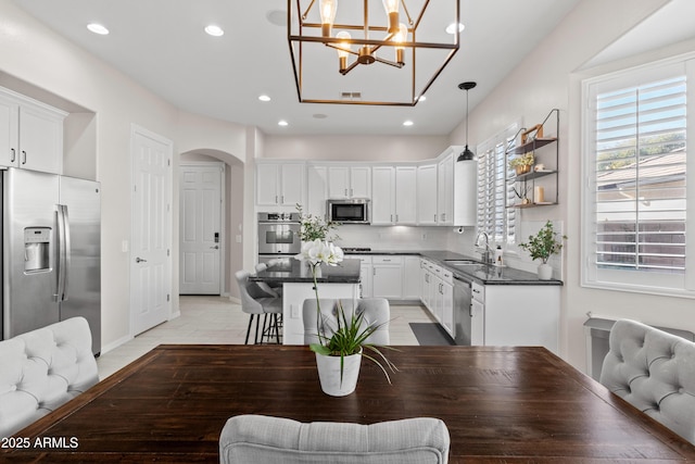 kitchen with arched walkways, a sink, white cabinetry, appliances with stainless steel finishes, and dark countertops