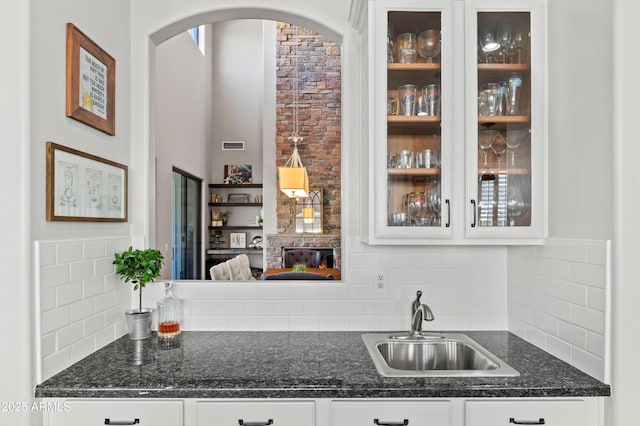 kitchen with visible vents, glass insert cabinets, a sink, white cabinetry, and backsplash