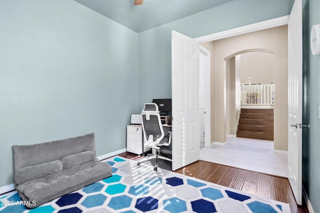 office space with arched walkways, wood finished floors, a ceiling fan, and baseboards