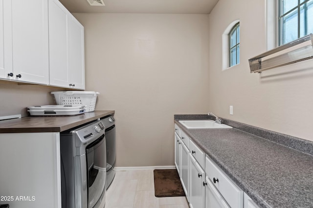 washroom featuring cabinet space, baseboards, visible vents, washer and clothes dryer, and a sink