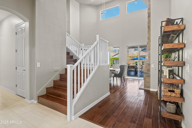 staircase featuring arched walkways, a high ceiling, wood finished floors, and baseboards