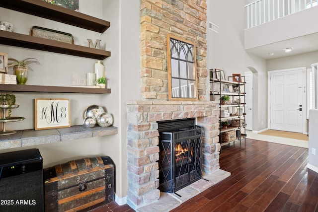 living room featuring arched walkways, visible vents, a stone fireplace, wood finished floors, and baseboards