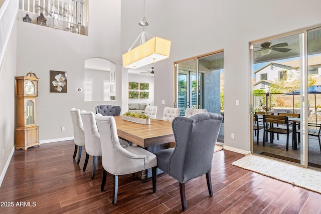 dining room with arched walkways, a towering ceiling, dark wood-type flooring, ceiling fan, and baseboards