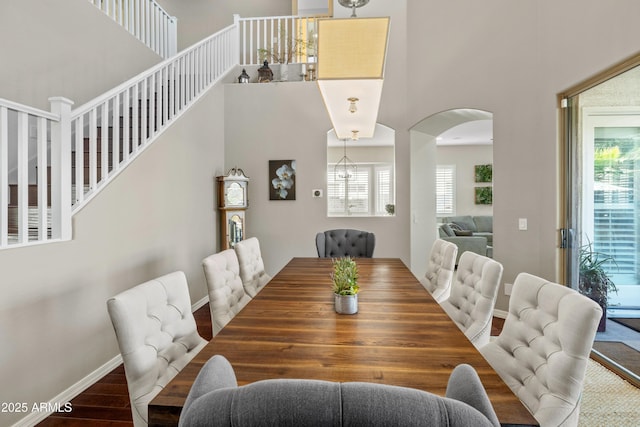 dining space featuring arched walkways, a high ceiling, wood finished floors, and baseboards