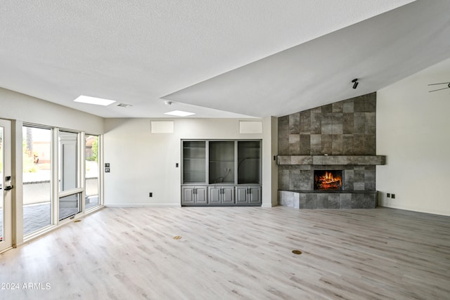 unfurnished living room with a textured ceiling, a tile fireplace, vaulted ceiling, and wood-type flooring