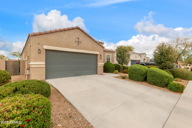 mediterranean / spanish home with a tiled roof, concrete driveway, stucco siding, an attached garage, and a gate