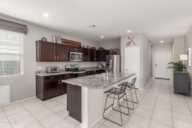 kitchen with visible vents, a sink, a kitchen breakfast bar, appliances with stainless steel finishes, and dark brown cabinets