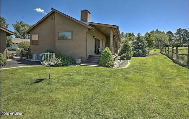 rear view of property with a lawn, a chimney, and fence