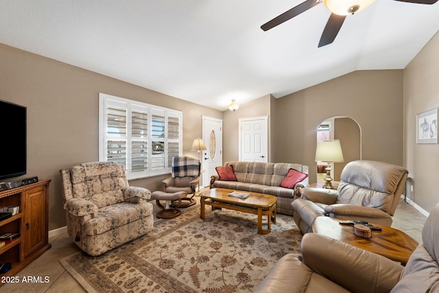 living area with arched walkways, a ceiling fan, vaulted ceiling, tile patterned flooring, and baseboards