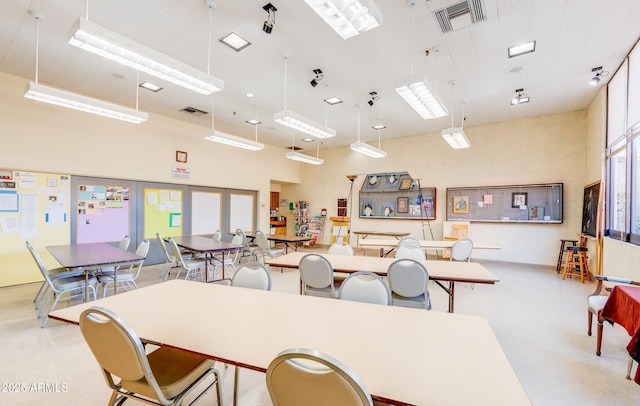 dining space featuring a towering ceiling, finished concrete floors, and visible vents