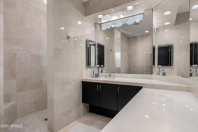 full bath with a walk in shower, double vanity, a sink, and tile walls