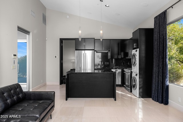 kitchen featuring stacked washer and clothes dryer, appliances with stainless steel finishes, dark stone countertops, dark cabinets, and plenty of natural light