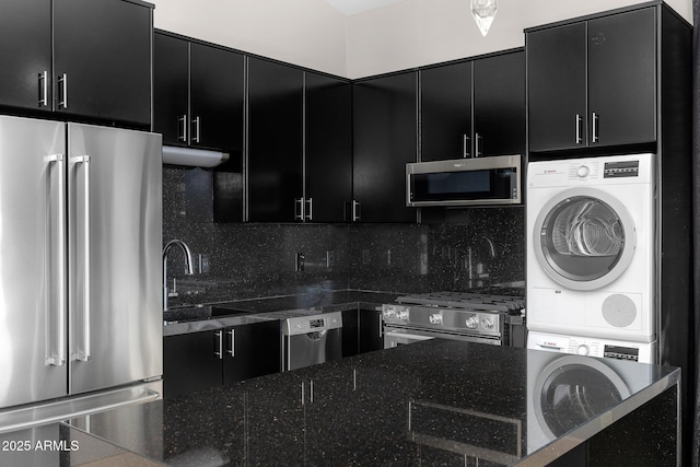 kitchen with tasteful backsplash, appliances with stainless steel finishes, a sink, stacked washing maching and dryer, and dark cabinetry