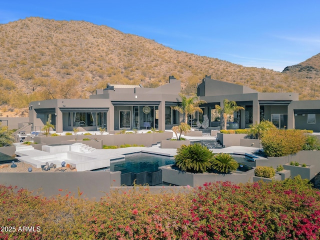 rear view of house with a fenced in pool, a patio area, a mountain view, and stucco siding