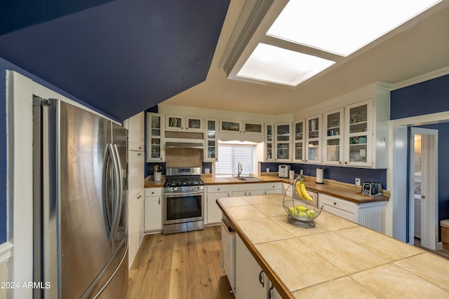 kitchen with white cabinets, appliances with stainless steel finishes, tile countertops, light hardwood / wood-style flooring, and sink