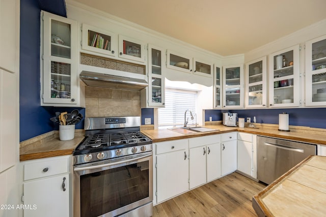 kitchen with sink, white cabinetry, stainless steel appliances, wall chimney exhaust hood, and light hardwood / wood-style flooring