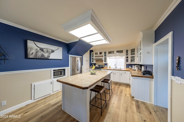 kitchen with appliances with stainless steel finishes, a kitchen island, light hardwood / wood-style floors, white cabinets, and ornamental molding