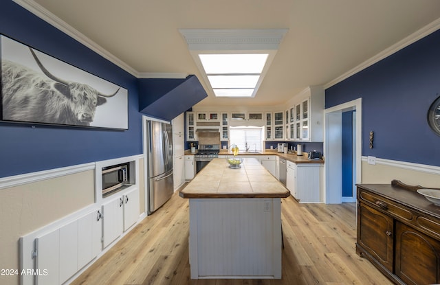 kitchen with a kitchen island, crown molding, white cabinetry, light wood-type flooring, and appliances with stainless steel finishes