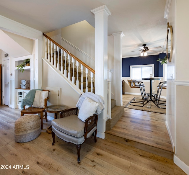 living area with decorative columns, crown molding, and light wood-type flooring