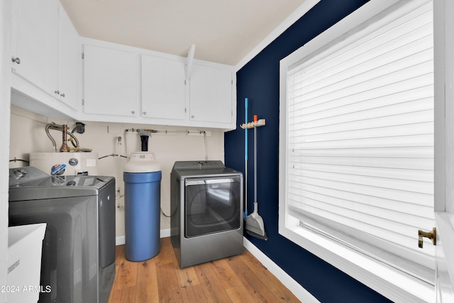 clothes washing area with light hardwood / wood-style floors, water heater, cabinets, and washing machine and clothes dryer