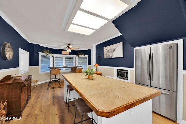 kitchen featuring a kitchen breakfast bar, stainless steel appliances, ornamental molding, light hardwood / wood-style floors, and ceiling fan