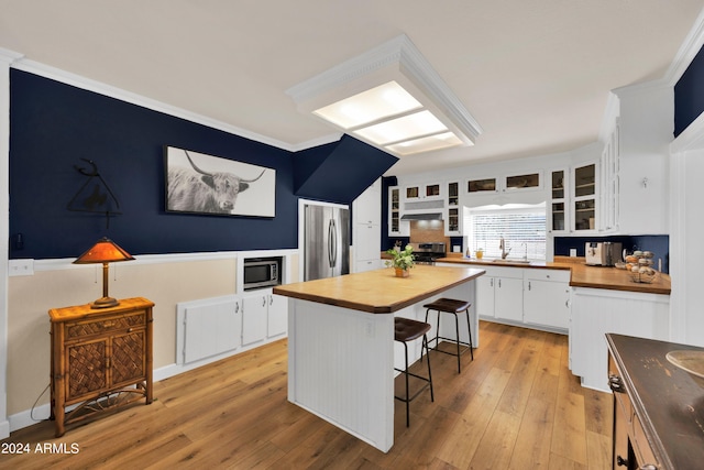 kitchen featuring butcher block counters, white cabinets, a kitchen bar, light wood-type flooring, and appliances with stainless steel finishes