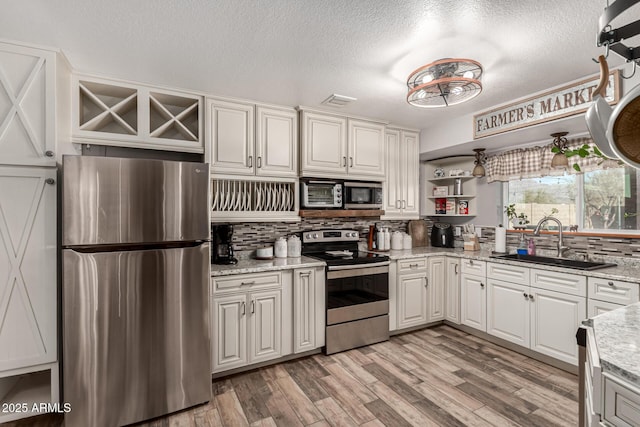 kitchen featuring tasteful backsplash, stainless steel appliances, light wood-style floors, open shelves, and a sink