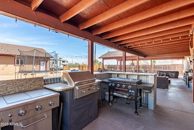 view of patio featuring exterior bar, a fenced backyard, grilling area, a trampoline, and exterior kitchen