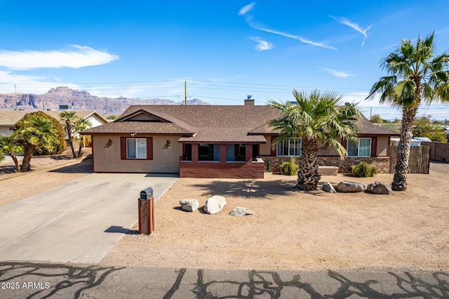 ranch-style home featuring driveway, roof with shingles, fence, a mountain view, and brick siding