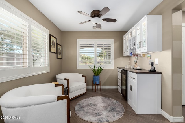 living area featuring a dry bar, beverage cooler, baseboards, dark wood finished floors, and ceiling fan