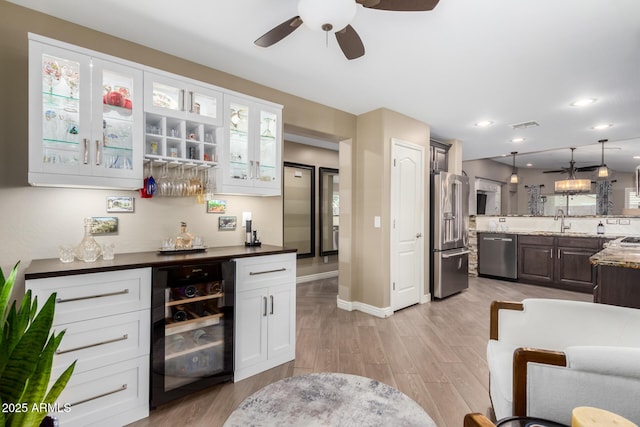 kitchen featuring beverage cooler, stainless steel appliances, a sink, light wood-type flooring, and glass insert cabinets