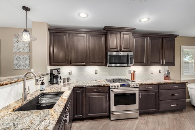 kitchen featuring dark brown cabinetry, a sink, light stone countertops, stainless steel appliances, and backsplash