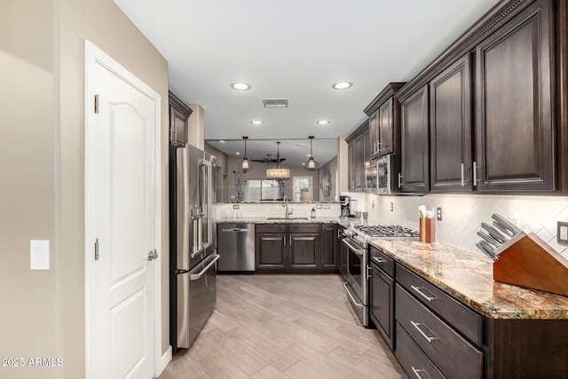 kitchen featuring stainless steel appliances, visible vents, dark brown cabinetry, and light stone countertops