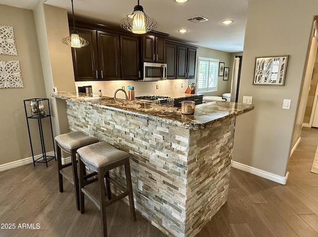 bar featuring decorative backsplash, visible vents, stainless steel appliances, and dark wood-type flooring