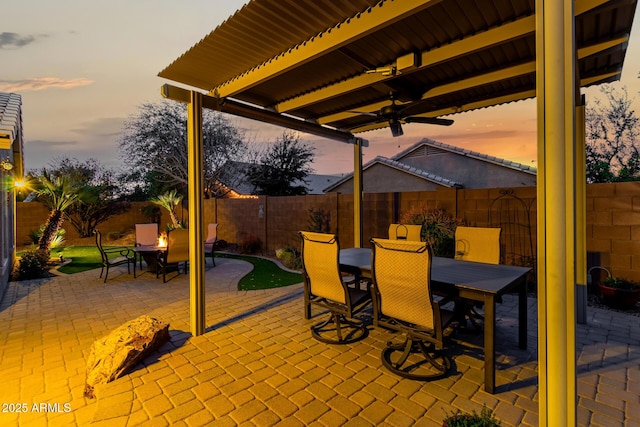 patio terrace at dusk featuring outdoor dining area, a fenced backyard, and ceiling fan