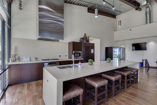 kitchen with a sink, wall chimney range hood, modern cabinets, light wood-type flooring, and built in appliances