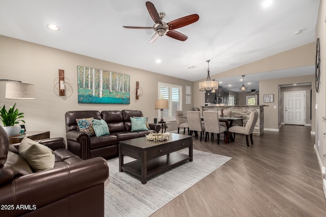 living area featuring lofted ceiling, recessed lighting, wood finished floors, baseboards, and ceiling fan with notable chandelier