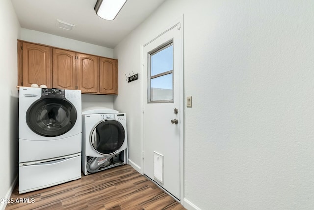 laundry room featuring wood-type flooring, washing machine and dryer, and cabinets