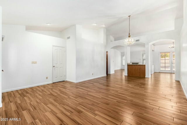 unfurnished living room featuring high vaulted ceiling, light hardwood / wood-style flooring, and a notable chandelier