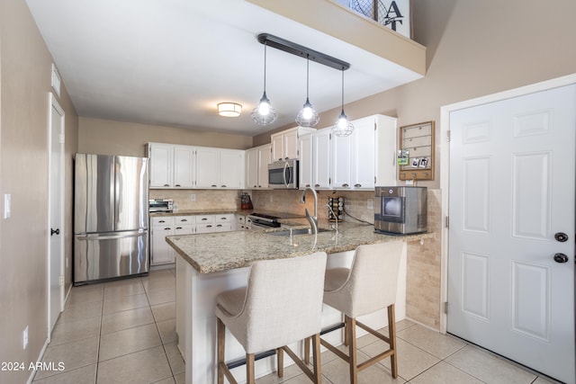 kitchen with light stone countertops, white cabinets, kitchen peninsula, and stainless steel appliances